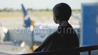 小男孩坐在机场候机楼的大窗户旁边看喷气式飞机的剪影视频